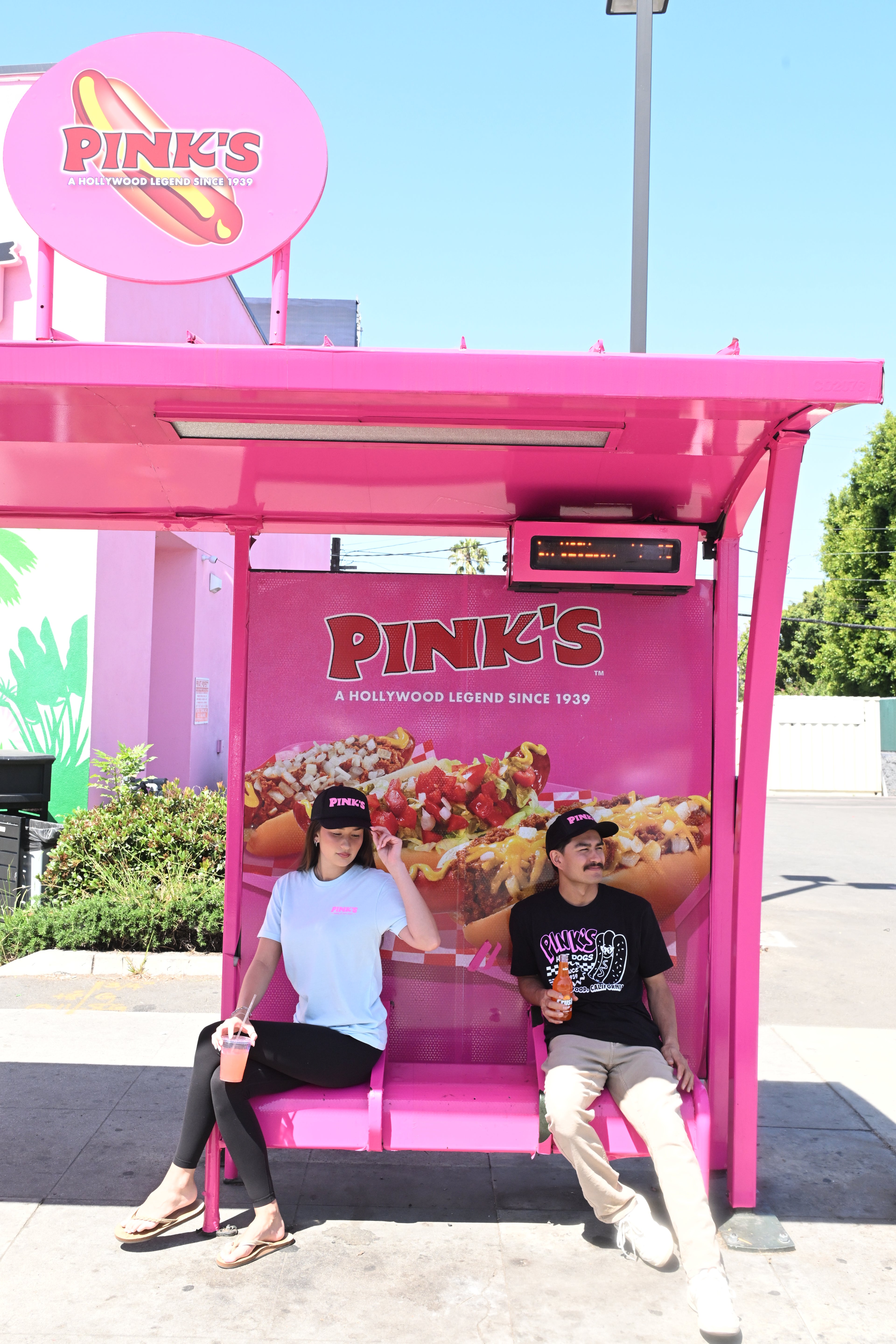 Two people wearing Pink's trucker hats and the Pink's Hollywood tee and Classic car tee